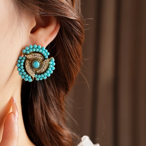 Detailed view of vintage gold flower swirl earring with turquoise and rhinestones on model