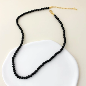 Detailed macro view of black onyx beads necklace with golden lobster clasp on white tray
