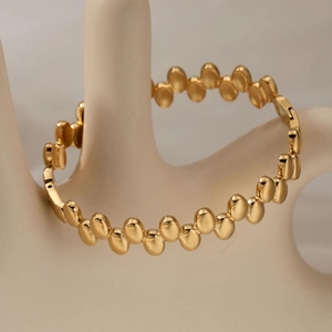 Polished gold stainless steel beaded oval bracelet for women displayed on a hand model