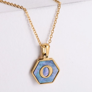 Close-up of hexagonal gold pendant with blue shell inlay and golden letter O detail