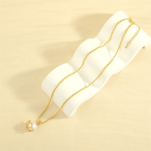 Close-up of a gold necklace with a white pearl pendant on a wavy display stand