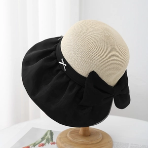 Detail of summer straw hat featuring contrast black mesh bow and wavy brim texture