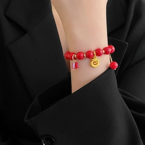 Détail du bracelet en perles rouges avec pendentif doré porte-bonheur au poignet d'un mannequin