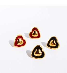 Close-up of heart-shaped earrings featuring red and black enamel with gold metallic frames