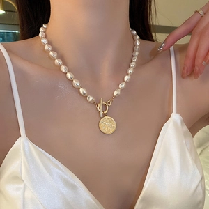 Close-up of pearl necklace with gold OT clasp and coin pendant on a model