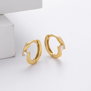 Detailed close-up of gold geometric huggie earrings with sparkling clear cubic zirconia
