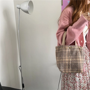 Detail of a vintage plaid woolen tote bag held by a model in a minimalist room.