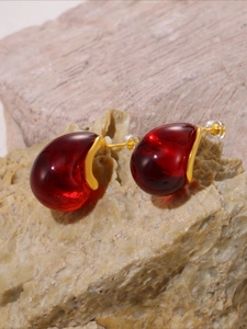 Detail of red candy-colored resin earrings with gold metal base on a stone background