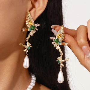 Detailed shot of bird-shaped gold earrings with colorful gems and teardrop pearl