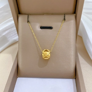 Detailed close-up of a gold cylinder pendant with radial texture on a fine cable chain