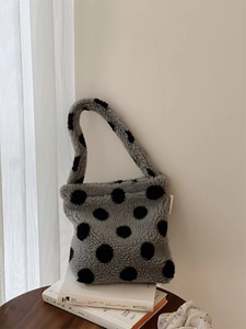 Sac à main en peluche à pois noirs sur fausse fourrure grise posé sur des livres