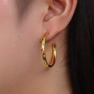 Close-up of golden C-shaped hoop earrings with colorful inlaid crystals on model
