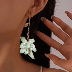 Close-up of golden branch earrings with mint green enamel flower pendant on model
