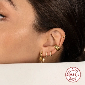 Detail view of gold S925 sterling silver hoop earrings with star and cross charms on ear
