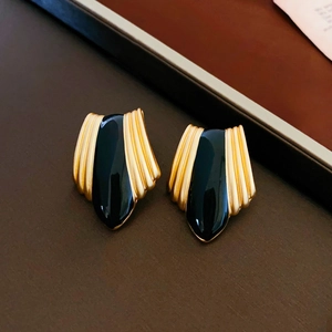 Macro detail of vintage gold and black enamel winged earrings on dark leather background