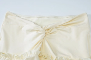 Detailed macro view of the twist knot waist and ruffled hem on a beige summer dress