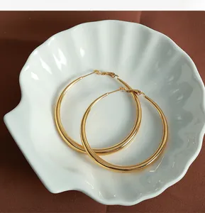 Détail de grandes boucles d'oreilles créoles dorées polies sur un plateau en coquillage
