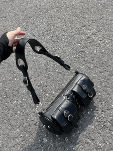 Detail of black cylindrical bag with metal eyelets and double front flap pockets