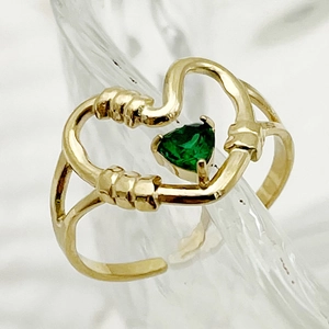 Detailed shot of golden heart chain ring with triangular green gemstone on glass surface