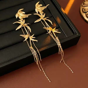 Detailed view of gold bamboo leaf earrings with long tassels on a professional jewelry stand