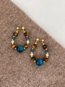 Gros plan de boucles d'oreilles artisanales avec œil de tigre et perles sur tricot
