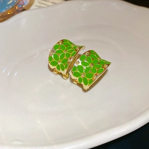 Macro shot of gold-plated C-shaped flower earrings with green enamel petals on white tray