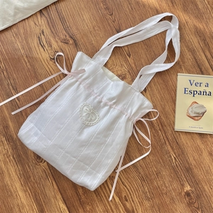 Detail of white drawstring tote bag with pink satin bows and heart-shaped embroidery