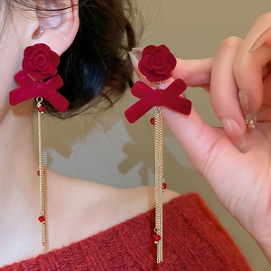Detail of red velvet bow earrings with flower accents and long golden tassels