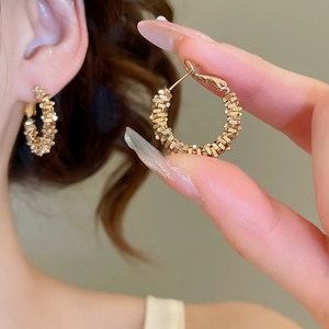 Detailed close-up of a gold-plated textured hoop earring worn on a model ear