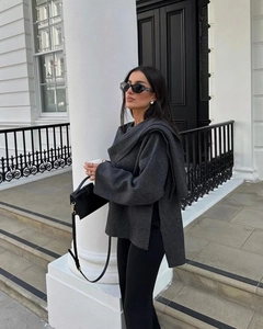Outdoor fashion shot of dark grey knit poncho sweater with matching scarf and black pants