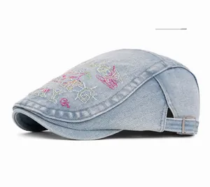 Detail view of washed denim flat cap featuring colorful embroidery and side metal buckle