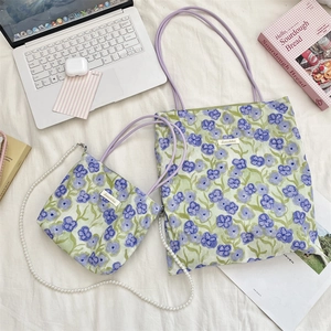 Dettaglio della borsa floreale con catena di perle e pochette su fondo in tessuto bianco
