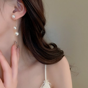Detail view of elegant gold S-curve tassel earrings with three gradient white pearls