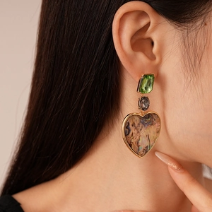 Primo piano di orecchini a cuore geometrici con trama abalone e cristalli verdi su modella