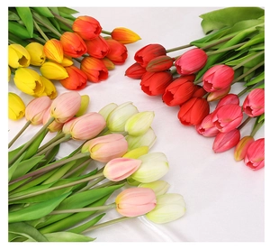 Flat lay of artificial tulip bouquet in yellow, orange, red and pink on white fabric