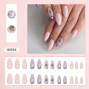 Almond press-on nails in nude pink with glitter accents and Little Angel letter designs