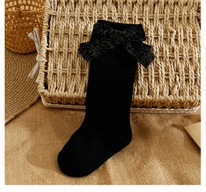 Detail of black knit baby socks featuring a large glittery bow on rustic linen
