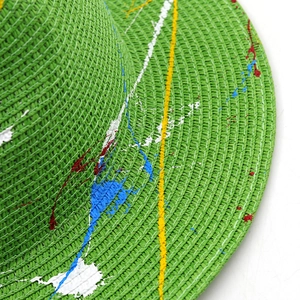 Close-up of green woven straw hat featuring artistic colorful paint splatter texture