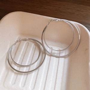 Détail de boucles d'oreilles créoles multicouches argentées sur un plateau texturé