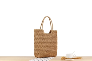 Close-up of a large khaki straw woven tote bag on a wooden table with home decor items