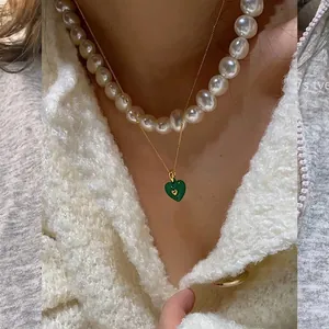Close-up of layered gold chain with green enamel heart pendant and white pearl necklace