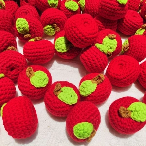 Handmade red crochet apple keychains with green leaves piled on a white background