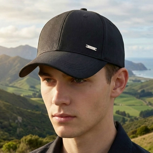 Man wearing a black corduroy baseball cap with metal logo plate in sunset outdoor scenery