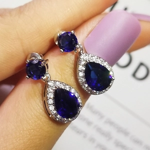 Macro shot of silver pear-cut blue sapphire earrings with pavé zircon accents held by hand