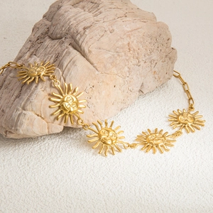 Detailed view of gold sun face charms on a stainless steel chain over a natural stone