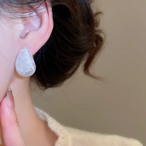 Macro view of teardrop resin stud earrings with white marble texture on ear model