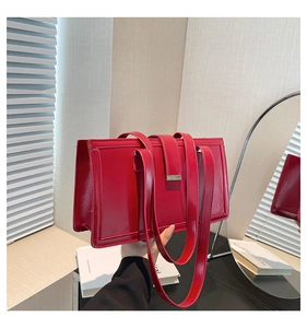 Detail of glossy bright red rectangular handbag with thin straps held by hand