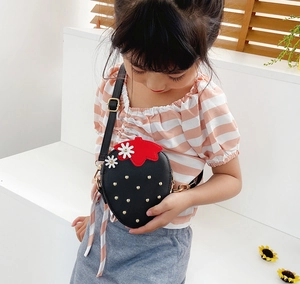 Girl wearing a black strawberry shaped crossbody bag with red leaves and white flowers