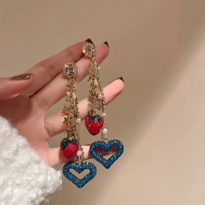 Close-up of dangling earrings with red diamond strawberry and blue heart charms