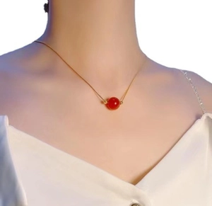 Detail of gold titanium snake chain necklace with a red agate bead on a model
